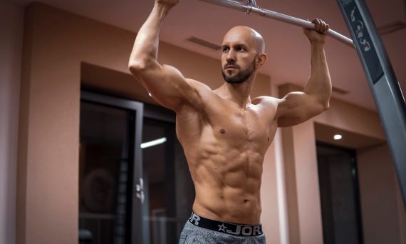 A bald, muscular man performing exercise on gym equipment indoors.